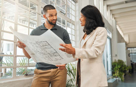 Businesswoman talking to an architect about blueprint. Colleagues brainstorm, collaborate on...