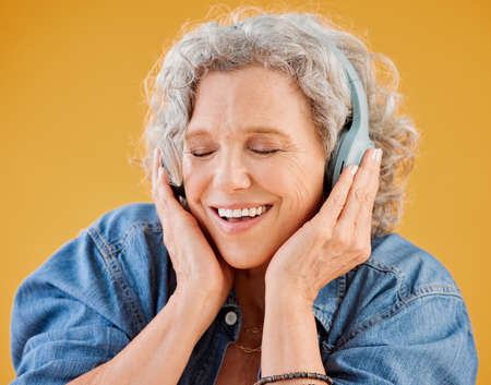 One happy mature caucasian woman wearing headphones and listening to music while dancing against a...