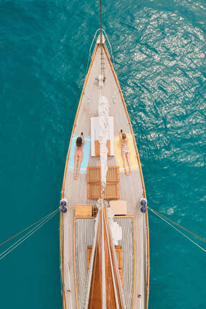 Two women in bikinis lying on yacht sunbathing using cellphones from above. Friends on holiday...