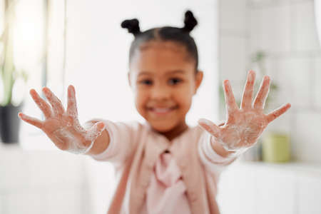 One mixed race adorable little girl washing her hands in a bathroom at home. A happy Hispanic child with healthy daily habits to prevent the spread of germs, bacteria and illnessの写真素材