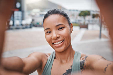 Sporty young mixed race woman with tattoos taking selfies while exercising. Happy young confident...