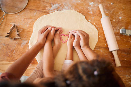 An unknown mother and daughter bonding while baking cookies in a kitchen at home. Unrecognizable mixed race family of two having fun while making shapes in doughの写真素材