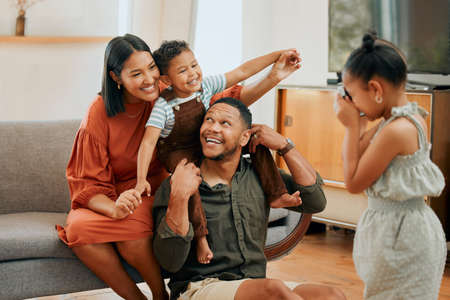 A happy mixed race family of four relaxing in the lounge and being playful together. Loving black family bonding with their kids while having a photo taken on the sofa at homeの写真素材