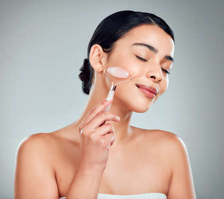 One beautiful mixed race woman using a rose quartz derma roller during a selfcare grooming routine. Young hispanic woman using anti ageing tool against grey copyspace backgroundの写真素材