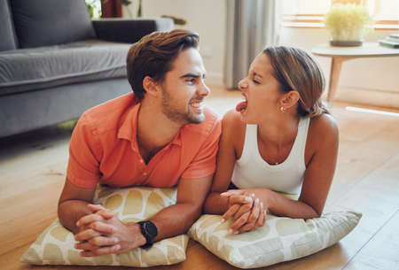 Funny romantic caucasian couple being playful pulling faces at each other while lying on the living...