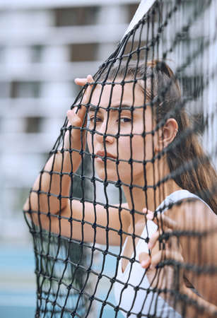 Close up of a female athlete leaning against a tennis net. Young hispanic tennis player posing on a tennis courtの写真素材