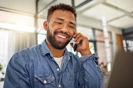 Happy businessman making a phone call at home. Young entrepreneur working from home on his laptop. Remote worker using his laptop and cellphone at home. Smiling handsome businessman at homeの写真素材
