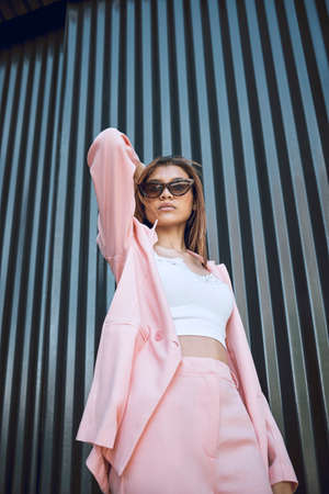 A young trendy and confident mixed race woman looking stylish while posing and spending time in the city. Fashionable hispanic woman wearing pink clothes and sunglassesの写真素材