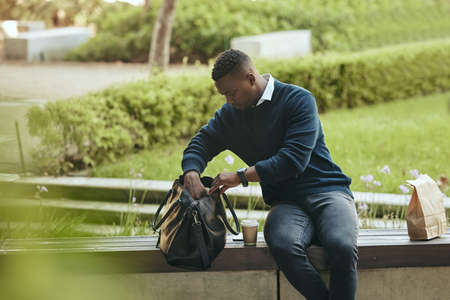 Businessman outside during his lunch break. Man checking his bag while sitting outside. Businessman...