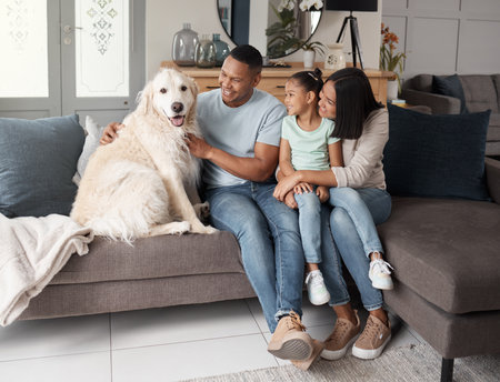 A happy mixed race family of three relaxing on the sofa with their dog. Loving black family being affectionate with a foster animal. Young couple bonding with their daughter and rescued puppy at homeの写真素材