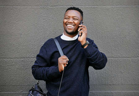 African american male on a phone call with his mobile device outside a building during the day while smiling Young black male talking on a phone while commuting to workの写真素材