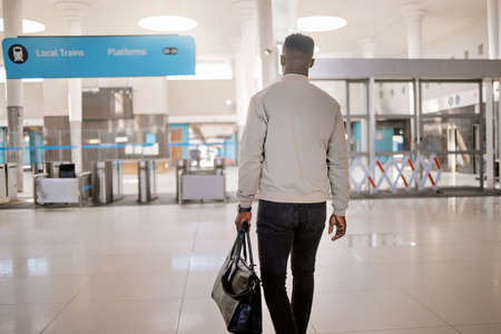 Rear view of African american businessman travelling alone and walking in a train station while...