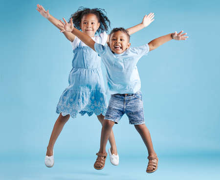Full length portrait of cute girl and boy jumping with their arms outstretched and having fun on...