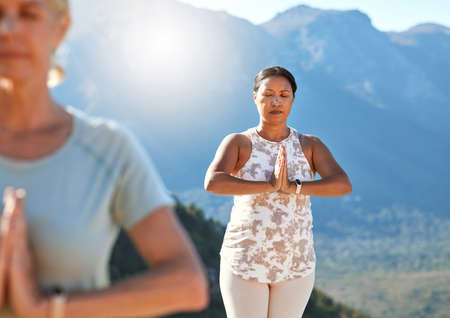 Mature woman meditating with joined hands and closed eyes breathing deeply. Mature people doing yoga together in nature on a sunny dayの写真素材