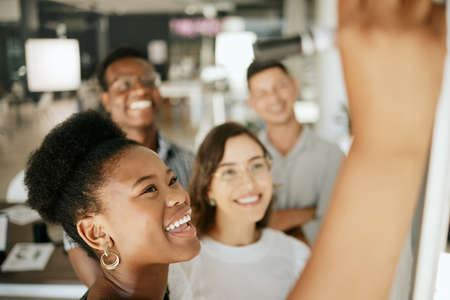 Happy african american business woman leader writing on board explaining idea and thoughts while brainstorming with colleagues. Diverse colleagues discussing ideas while collaborating on projectの写真素材