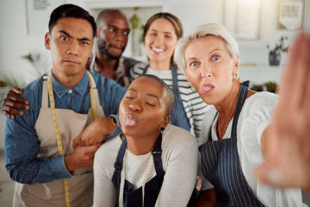 Portrait of a group of five diverse creative clothing designers taking a silly selfie together while at work. Mature caucasian female tailor taking a photo with her colleagues working at a boutiqueの写真素材