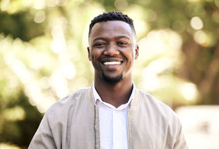 Portrait of a young businessman standing in the street in the city smiling and looking happy on a sunny day. African american male expressing happiness on his faceの写真素材