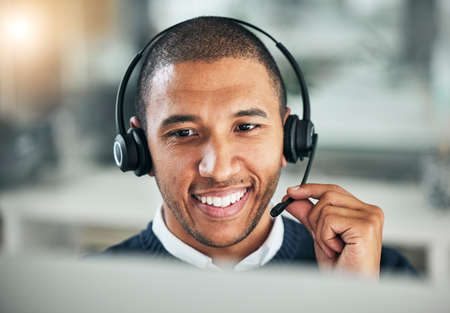 Young mixed race male call centre agent talking on a headset while working on a computer in an...