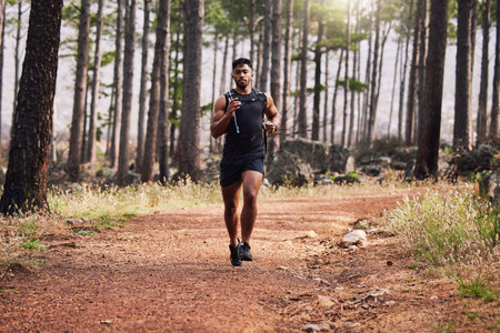 Young mixed race fit male athlete running in a forest outside in nature. Exercise is good for health and wellbeing. Jogging in a park alone during the dayの写真素材