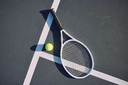 Tennis racquet and ball on an empty sports court outside from above on a sunny day. Sports gear and equipment for leisure or a professional player. A hobby that promotes exercise, fitness and wellnessの写真素材