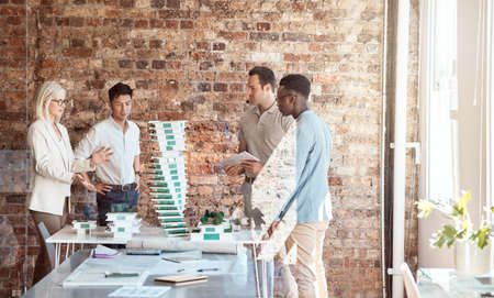 Group of diverse architects discussing plans, blueprints and schematics during a meeting in their...
