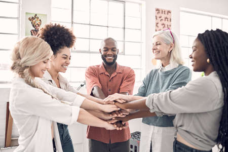 Group of five cheerful diverse businesspeople piling their hands together in an office at work....