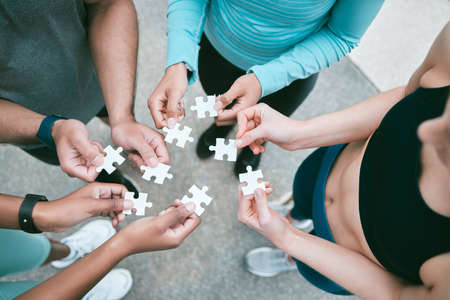 Closeup of diverse group of people from above assembling jigsaw puzzle pieces together. Hands of multiracial people working in synergy to problem solve. Using dedicated teamwork to support and help find common solutions.の写真素材