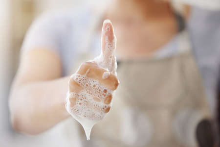 An unrecognizable woman with foam covered hands showing the thumbs up gesture. One unknown woman...
