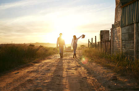 Two farmers carrying a basket of fresh produce and walking against a sunset background. Unrecognisable woman celebrating successful harvest on a farm with male colleagueの写真素材