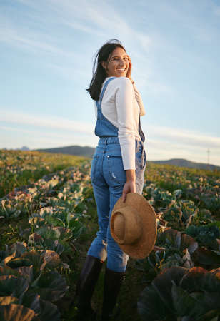 Portrait of a woman farmer standing in a cabbage field on a farm. Young female with a straw hat and rubber boots looking over her field of organic vegetablesの写真素材