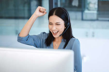 Youll thrive if you keep at it. Shot of a young call centre agent cheering while working on a computer in an office.の写真素材