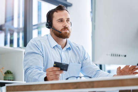 Waiting for payment confirmation. Shot of a young call centre agent using a credit card while...