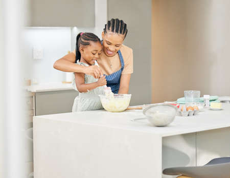 Youll want to mix it slowly. Shot of an attractive young mother bonding with her daughter and helping her bake in the kitchen at home.の写真素材