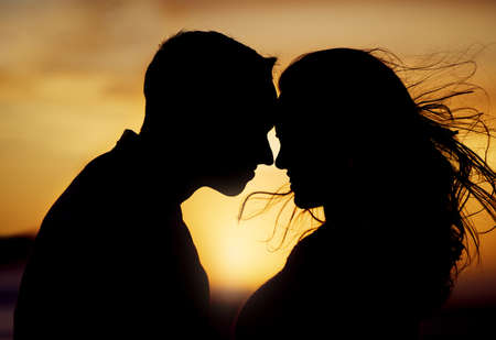 Silhouette couple enjoying romantic moment with their foreheads touching against sunset background. Unknown boyfriend and girlfriend feeling in love while bonding outside. Man and woman gently huggingの写真素材