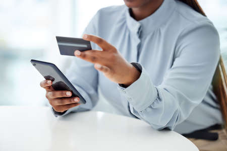 Businessperson using a credit card and phone to shop online at work. One person paying for a...