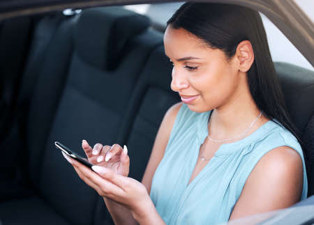 One young beautiful mixed race businesswoman typing a message on a phone while sitting in a car....