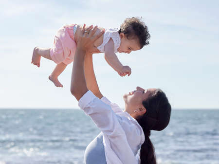 Mother lifting a baby. Mother and daughter on holiday by the ocean. Happy mother playing with her...