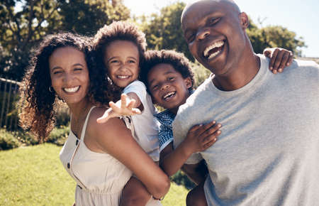 Cheerful young african american parents playing with their little sons in the garden. Excited mother and father carrying their sons on piggyback rides. Smiling couple enjoying a day in the parkの写真素材