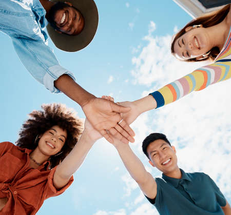 Low angle view of diverse group of people standing huddled together with hands piled in the middle....