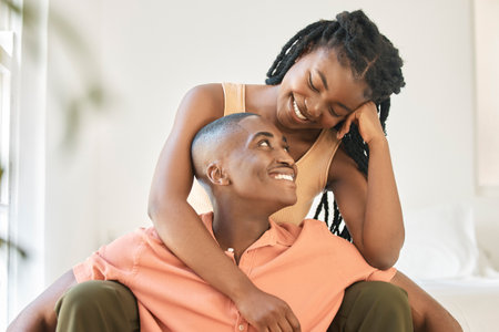 Young happy carefree and cheerful african american couple bonding and enjoying relaxing time together at home. Loving black female smiling while hugging and looking at her boyfriend sitting togetherの写真素材