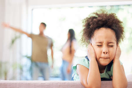 Shot of a little girl covering her ears while her parents argue in the background.