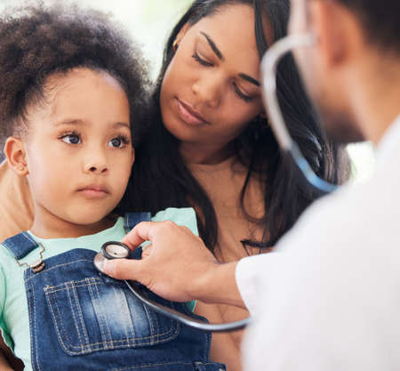 Shot of a little girl sitting on her mothers lap while being examined by her doctor.の写真素材