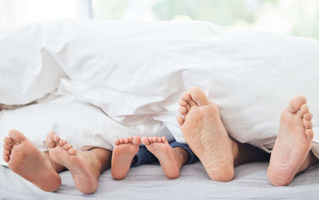 The comfiest place in the world. Cropped shot of a little girl lying between her mother and father on their bed.の写真素材