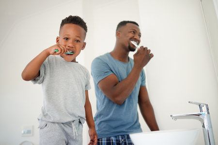 Portrait of a little boy brushing his teeth with his father in the bathroom at home.の写真素材