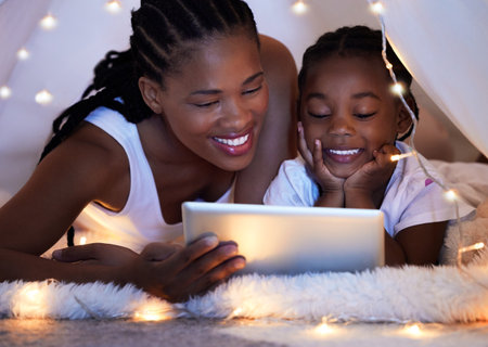 Shot of a mother and her daughter using a digital tablet together while relaxing under a blanket fort at home.の写真素材