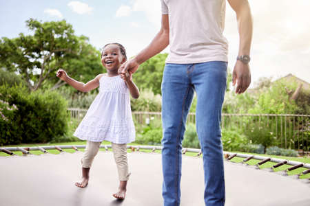 Ill hold you hand so you can jump high. Shot of a little girl jumping on a trampoline with her father outdoors.の写真素材