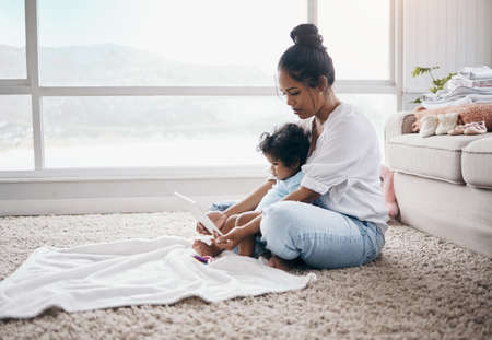 Time for cartoons. Full length shot of a young woman sitting in the living room with her daughter and using a digital tablet.の写真素材