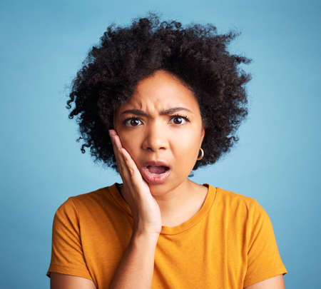 Oh my goodness. Shot of an attractive young woman standing alone against a blue background in the studio and looking shocked.の写真素材