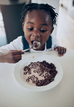 A daughter is a gift of love. Shot of an adorable little girl sitting alone in the kitchen and eating his breakfast.の写真素材