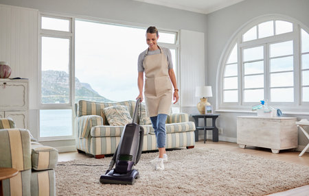 Freshening up her home. Shot of a young woman vacuuming a carpet in the lounge at home.の写真素材